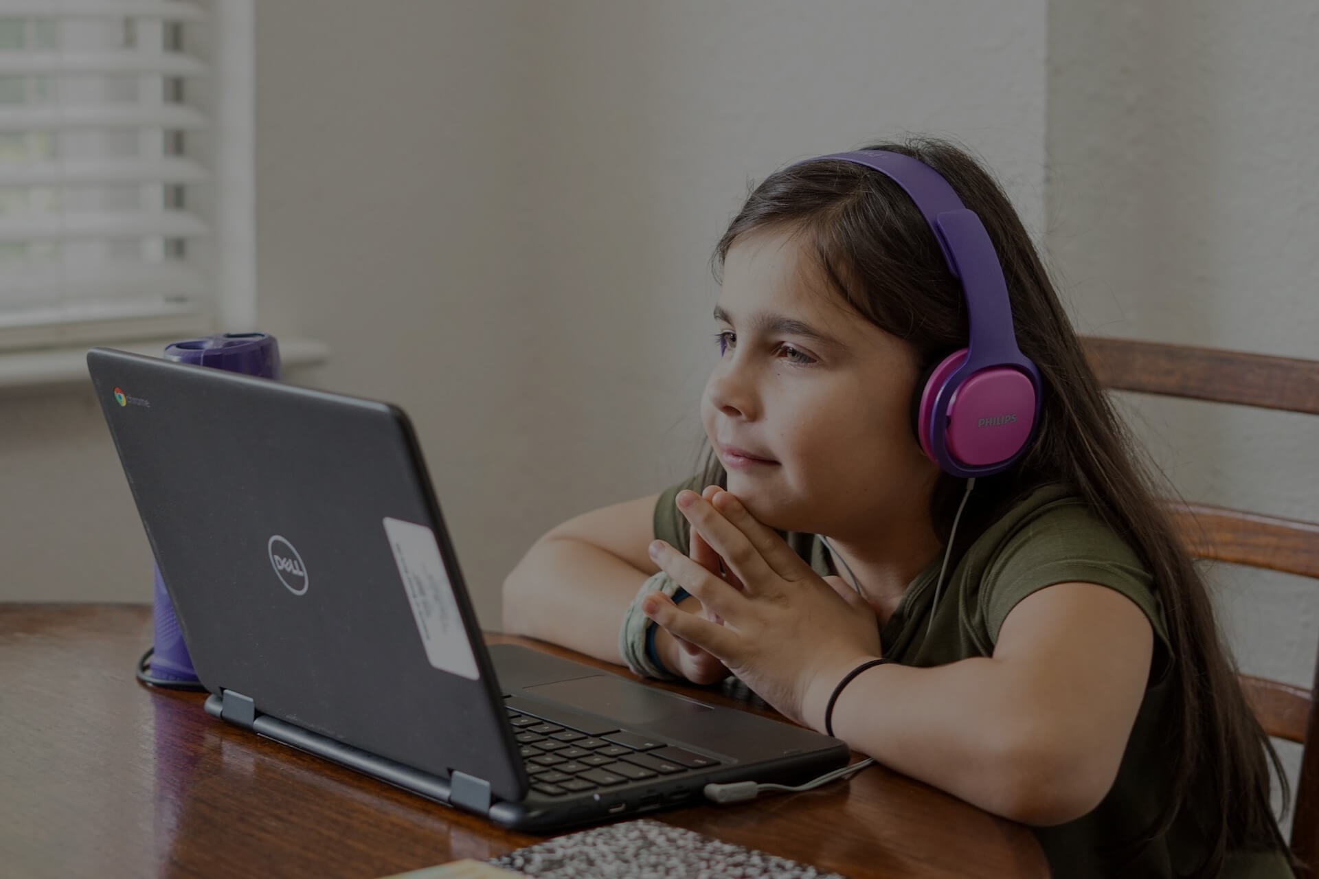 Background image for ClassDojo case study hero section, A girl wearing headphones, watching an online class on a convertible laptop