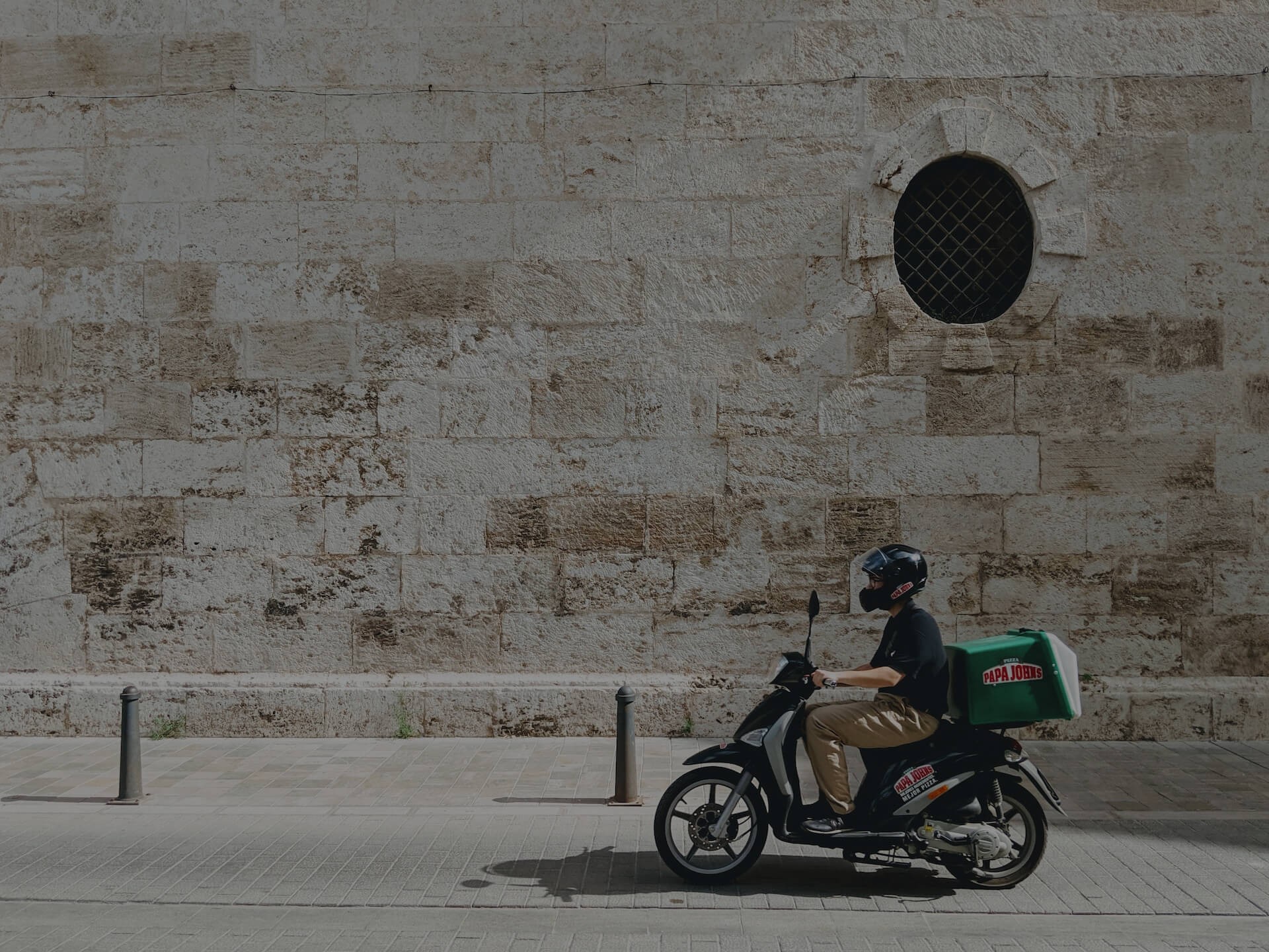 Background image for Habitat Logistics case study hero section, A delivery worker on a motorcycle seen from the side, carrying an order for a pizzeria